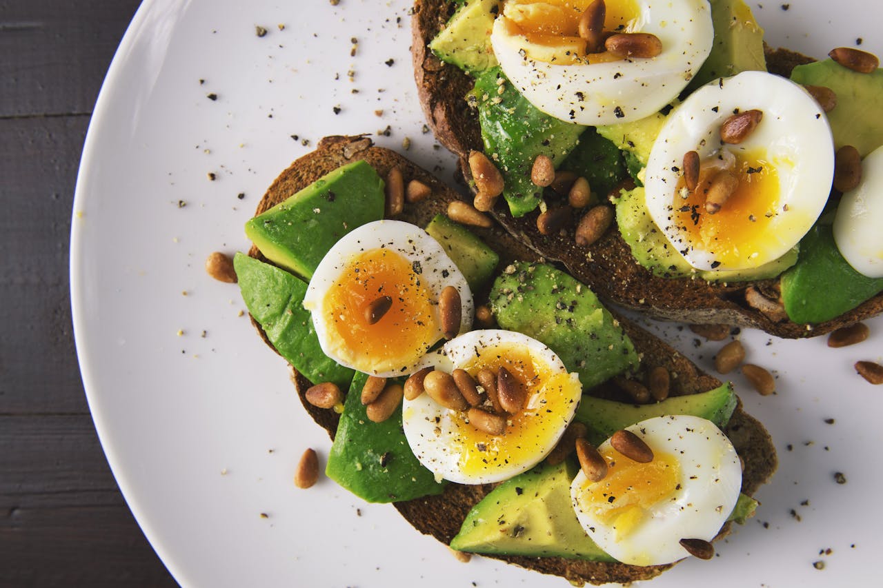 our-services-1 Delicious avocado toast topped with soft-boiled eggs and pine nuts on a white plate.